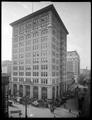 Wells Fargo building at corner of 6th and Oak, Portland. Delivery wagon and pedestrians in street, Hotel Irving in foreground.