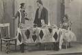 Three men (two dressed as women) on stage presenting a play