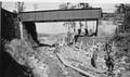 CCC crew working on rock wall next to creek, below a railroad bridge