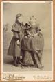 Two girls wearing dark dresses, one standing, the other sitting on a tall stool