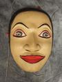 Theatrical mask of carved wood with painted eyes, lips, and hair in red, black, grey, and white on a beige skin ground