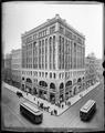 Dekum Building, Portland, on corner of 3rd and Washington. Street cars and pedestrians painted in on streets and sidewalk. Elevated perspective.