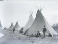 People standing and sitting outside of tepees