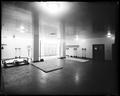 Gymnasium room with exercise equipment, mats, etc. Identified as room in US National Bank, Portland. Scale against rear wall.