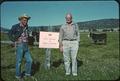 Gene Cross with man by sign on fence