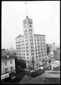 Full view of Oregonian Building, Portland, from intersection, 6th and Alder St. Horse-drawn delivery wagons in front of building. Power lines over street.