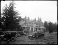 Large hotel at Flavel, OR., surrounded by trees. Autos parked in foreground.