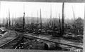 Smith Powers logging camp.  Railroad tracks ""Y"" in front of logging debris. Many upright snags & stumps. Barrel in foreground.