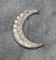 Pin of silver crescent moon with rhinestones and swirl design along edge