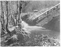 View of man sitting at bottom of stairs along trail with car in background. See 02-231.