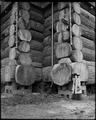 Close-up of log-joining at corner of Forestry Building, Lewis & Clark Exposition site, with wood block base. Woman standing at right of base-work of building.