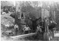 A logging crew gets their picture taken next to a one log load.  A sled mounted gasoline donkey sits behind the wooden spar tree.  This logging show was on Eckman Creek.