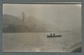 Two individuals rowing a boat with hills in the background, circa 1910