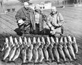 Three people on a dock with their fishing catch