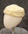 Large pillbox-style hat of ivory organdy composed of layered folds in a rectangular design