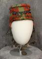Hat of red and green felt with a round metal disc on the flat crown and metal chains, turquoise colored beads and coins