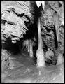 Man kneeling by stalagmite at entrance to Joaquin Miller's Chapel, Oregon Caves, OR.