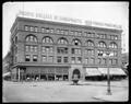 Front view of Commonwealth Building on 6th St., Portland. Safe and piano stores on sidewalk level. Chiropractic School sign on roof. Street with fountain in foreground.