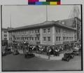 Hotel Scott, Broadway and Ankeny, Portland. Building decorated with flags. Tire stores, gas stations on ground level. Autos, gas truck in street. Advertisements for Carnation products and United States profit sharing coupons. (recto)