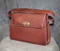 Handbag of reddish-brown leather in a rectangular shape with fold-over flap and brass twist closure at front center-bottom