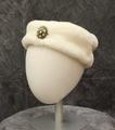 Pillbox hat of white faux fur with brass and rhinestone broach at center-front
